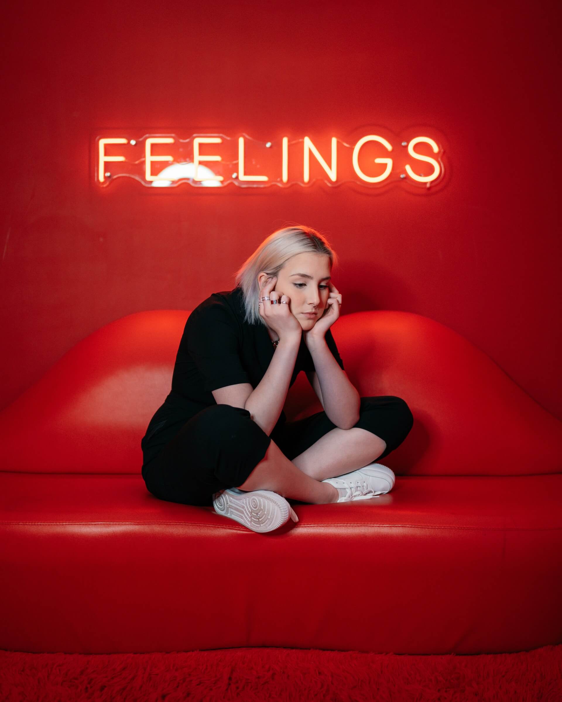 Czerwony neon Feelings nad smutną dziewczyną siedzącą na czerwonej kanapie.